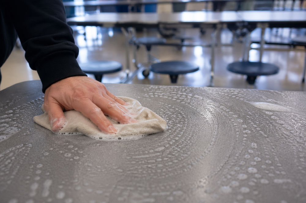 Close-up of cleaning a commercial cafeteria table with soapy water and cloth to maintain hygiene and durability in dining areas